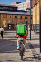 Rear view of a courier with thermo bag riding bicycle along tiled street on a sunny day
