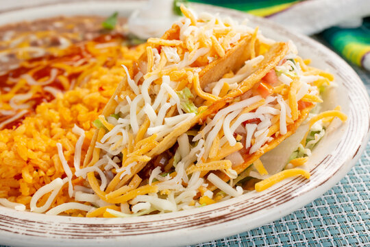 A closeup view of a plate of hard shell tacos, with rice and beans.