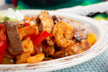 A closeup view of mixed meat fajitas on a plate, featuring shrimp, steak and chicken.