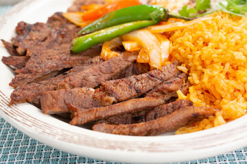 A view of a plate of carne asada slices, with rice and beans.