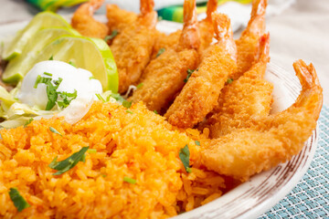 A closeup view of a plate of deep fried butterfly shrimp and a side of rice.