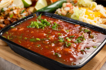 A closeup view of a container full of red salsa, in a restaurant or kitchen setting.