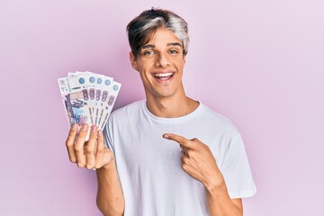 Young hispanic man holding russian 500 ruble banknotes smiling happy pointing with hand and finger