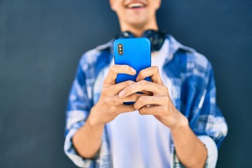 Young hispanic man smiling happy using smartphone and headphones at the city.