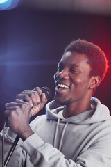 Vertical portrait of young African-American man singing to microphone passionately while standing on stage in lights