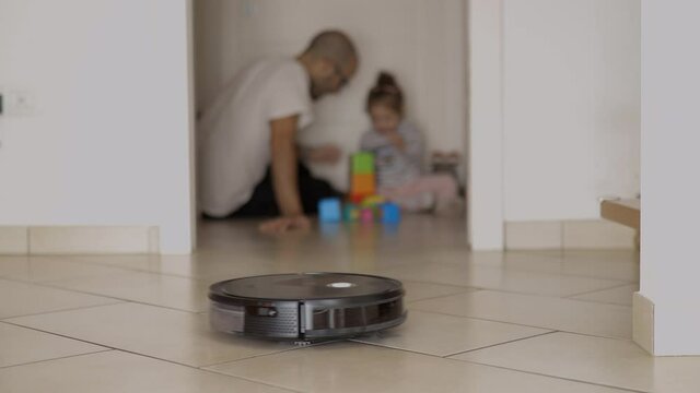 Cleaning robot does housework meanwhile father plays with his child. Machine cleans house for have more leisure in family. Man plays with his baby