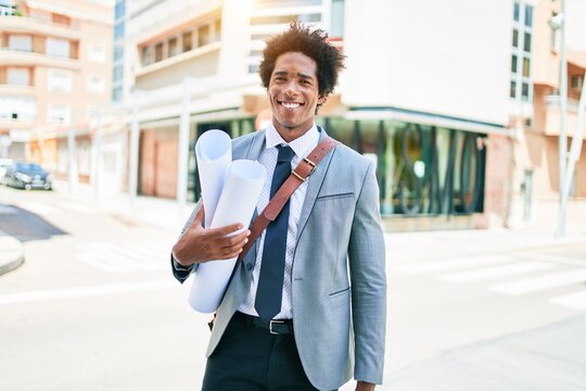 Young handsome african american architect man smiling happy. Standing with smile on face holding blueprints walking at town street. - Powered by Adobe