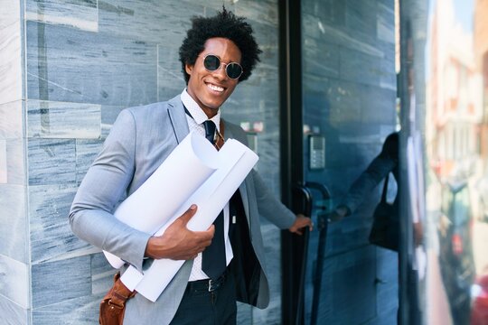 Young handsome african american architect man smiling happy. Standing with smile on face holding blueprints at the office door.