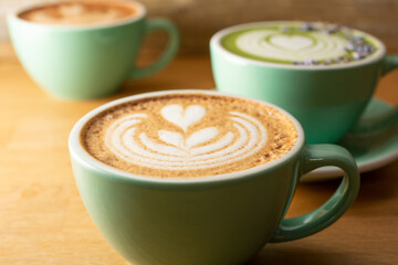 A view of several coffee latte art mugs on a wooden surface.