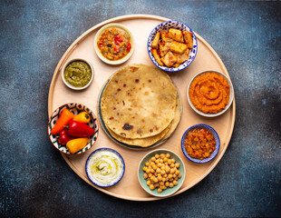 Indian Thali - selection of various dishes served on round wooden platter. Assorted Indian vegetarian meze with traditional chapati bread, paneer, dal, chutney in different bowls. Top view