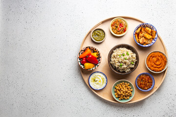 Indian Thali - selection of various dishes served on round wooden platter. Assorted Indian vegetarian meze with boiled basmati rice, paneer, dal, chutney in different bowls. Top view, space for text