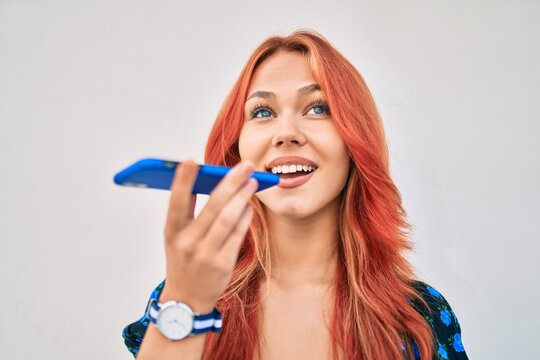 Young redhead girl smiling happy sending voice message using smartphone at the city.