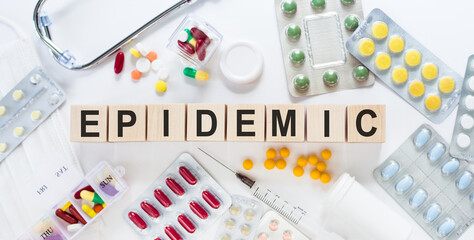 The word EPIDEMIC on wooden blocks on the table. Medical concept with pills, vitamins, stethoscope and syringe in the background.