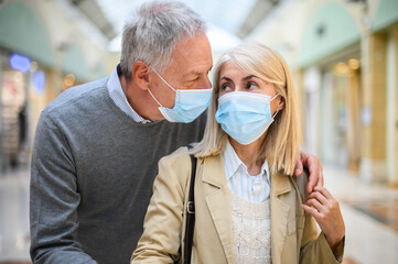 Senior couple shopping in a mall at coronavirus times, wearing masks