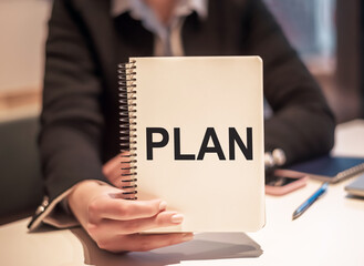 Business woman holds a notebook with the text PLAN.