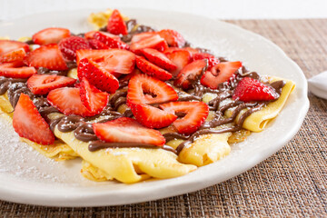 A view of crepes on a plate, topped with hazelnut chocolate spread and strawberry slices.