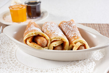 A view of a casserole dish with breakfast sausage links wrapped in pancakes, known as pigs in a blanket.