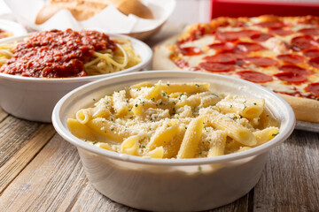 A view of several prepared Italian restaurant entrees, featuring penne Alfredo, spaghetti, and a pepperoni pizza.
