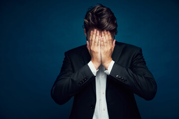 Portrait of depressed businessman hiding head in hands against dark blue background