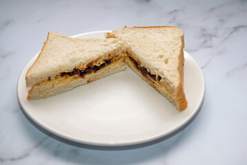 A close up of a cheese and Branston pickle sandwich on white bread on a white plate on a marbled white work top