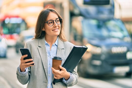 Young hispanic businesswoman using smartphone and drinking take away coffee at the city.
