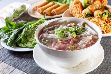 A view of a table full of a variety of Vietnamese dishes, featuring pho.