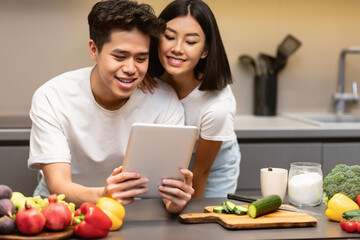 Japanese Couple Cooking Using Tablet Computer In Kitchen