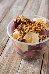 A view of an acai cup or bowl on a wooden table surface, featuring fruit and granola toppings.