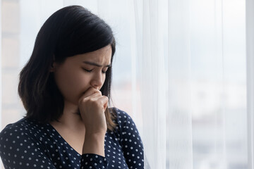 Fototapeta premium Close up frustrated Asian young woman standing near window, thinking about personal problems, crying, suffering from break up with boyfriend or divorce, melancholic female lost in thoughts