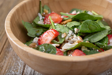 A closeup view of a spinach salad, featuring walnuts, feta, and strawberries.