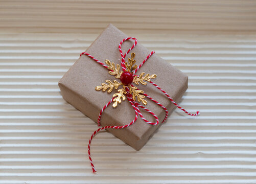Present box wrapped in brown kraft paper and red string. Decorated with berry and gold snowflake. Cream corrugated background and copy space for text. Concept Christmas festive gift giving