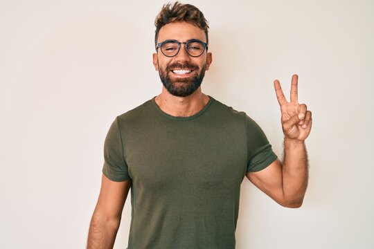 Young hispanic man wearing casual clothes and glasses smiling with happy face winking at the camera doing victory sign. number two.