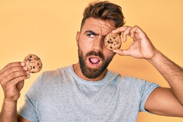 Young hispanic man holding cookie angry and mad screaming frustrated and furious, shouting with anger. rage and aggressive concept.