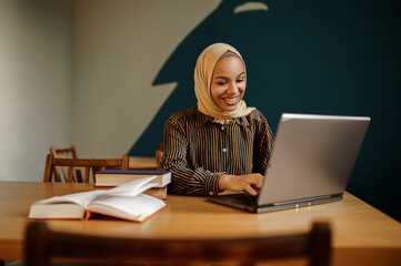 Arab female student in hijab using laptop in cafe
