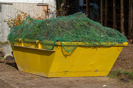 Eine gelbe Mulde, Container wird mit Bauschutt und Holz beladen.