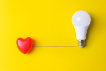 Red heart with Led light bulb on a yellow background. oncept of the origin of the idea from the...