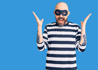 Naklejka premium Young handsome man wearing burglar mask celebrating crazy and amazed for success with arms raised and open eyes screaming excited. winner concept