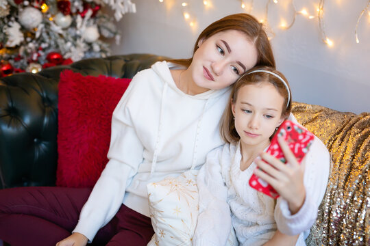 Two Pretty Sisters Of Fifteen And Eight Years Old Take Selfies, Talk On The Phone In The Christmas Interior