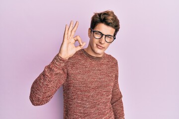 Handsome caucasian man wearing casual sweater and glasses smiling positive doing ok sign with hand and fingers. successful expression.