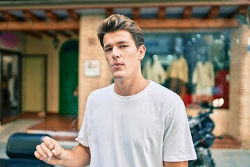 Young caucasian man with serious expression smoking cigarette at the city.