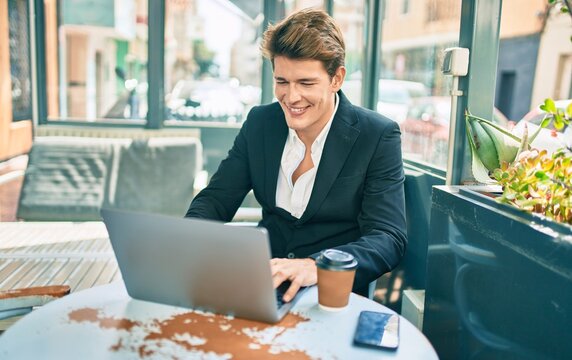 Young caucasian businessman smiling happy working using laptop at coffee shop terrace.