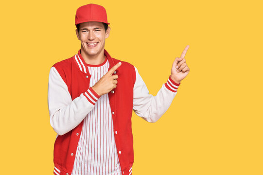 Handsome caucasian man wearing baseball uniform smiling and looking at the camera pointing with two hands and fingers to the side.