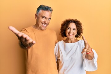 Beautiful middle age couple together wearing casual clothes smiling friendly offering handshake as greeting and welcoming. successful business.