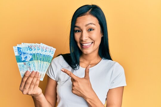 Beautiful hispanic woman holding hong kong 20 dollars banknotes smiling happy pointing with hand and finger