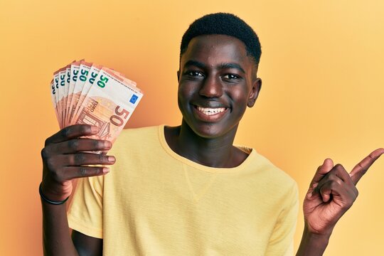 Young african american man holding 50 euro banknotes smiling happy pointing with hand and finger to the side