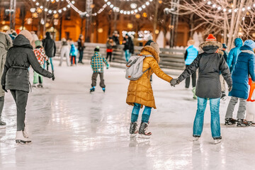 Happy couples, friends ice skate on a skating rink in a city park together. Healthy winter outdoor...