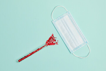 New Year's composition of a mask and a test tube with sparkles imitating blood on a light mint background. Top view, flat lay. Medical new year concept