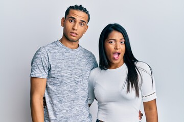 Young latin couple wearing casual clothes in shock face, looking skeptical and sarcastic, surprised with open mouth