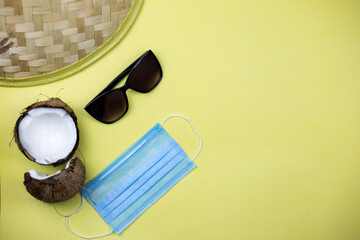 Triangular hat, coconut, mask and sunglasses lie on a yellow background. Vacation and tourism during quarantine and pandemic