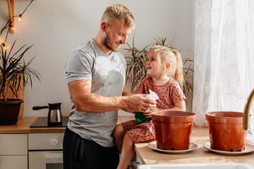 A happy little girl and a man splash water on a home flower. Father and daughter at home. Plant care.